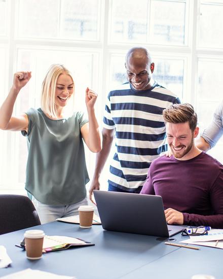 Fünf Personen in einem Büro feiern gemeinsam vor einem Laptop, sichtbar erfreut und motiviert