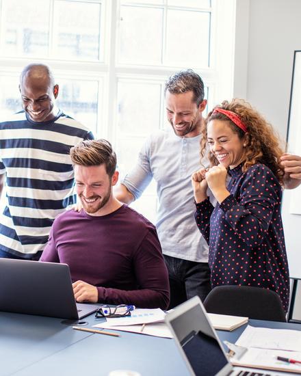 Fünf Personen in einem Büro feiern gemeinsam vor einem Laptop, sichtbar erfreut und motiviert
