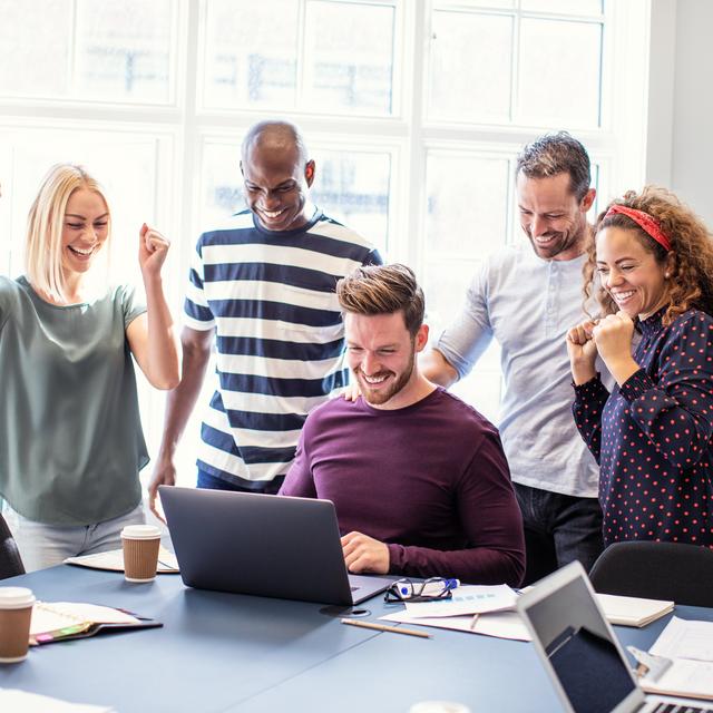 Fünf Personen in einem Büro feiern gemeinsam vor einem Laptop, sichtbar erfreut und motiviert