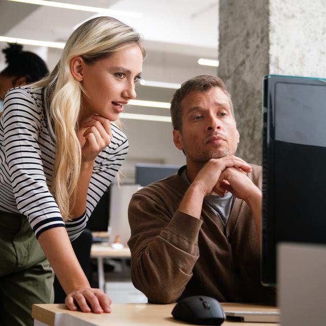 Zwei Kollegen arbeiten konzentriert gemeinsam an einem Computer in einem modernen Büro
