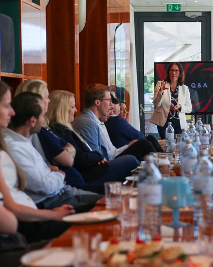 NextGen_MeettheCFO_05_2025 Frau präsentiert vor einer Gruppe von Menschen in einem Meetingraum mit Bildschirm, der 'Q&A' zeigt